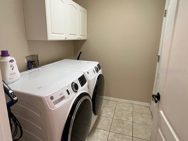 clothes washing area with light tile patterned floors, separate washer and dryer, baseboards, and cabinet space