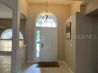 entryway featuring arched walkways, baseboards, a chandelier, a high ceiling, and light tile patterned flooring