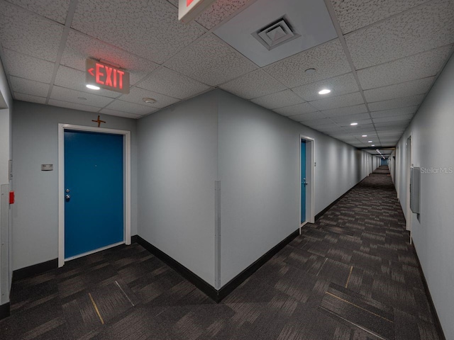 corridor featuring dark carpet, recessed lighting, a drop ceiling, and baseboards
