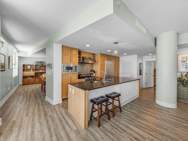 kitchen featuring built in appliances, a sink, light wood-style flooring, an island with sink, and recessed lighting