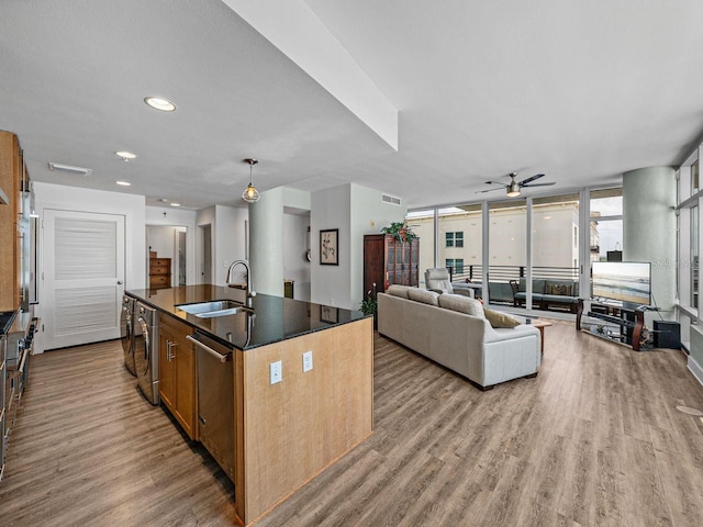 kitchen with a sink, wood finished floors, ceiling fan, an island with sink, and stainless steel dishwasher
