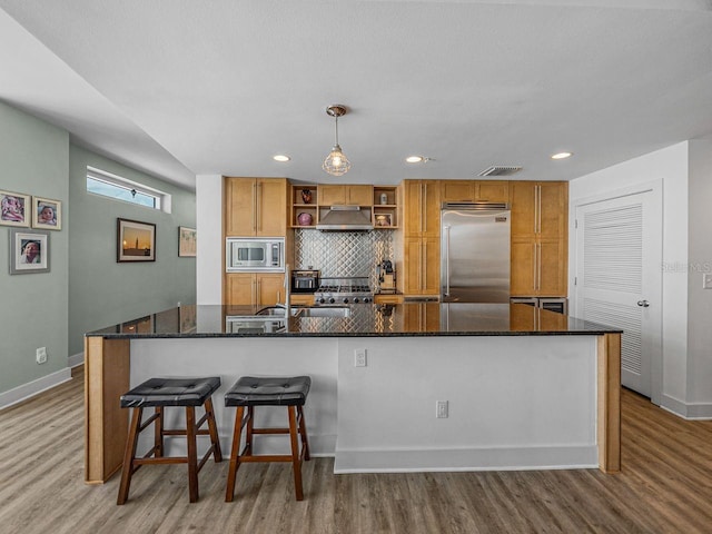 kitchen featuring built in appliances, under cabinet range hood, wood finished floors, tasteful backsplash, and recessed lighting