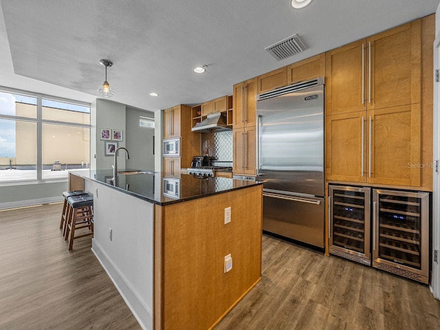 kitchen featuring built in appliances, a sink, beverage cooler, baseboards, and dark wood-style floors