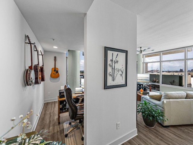 hallway featuring wood finished floors, an office area, and baseboards