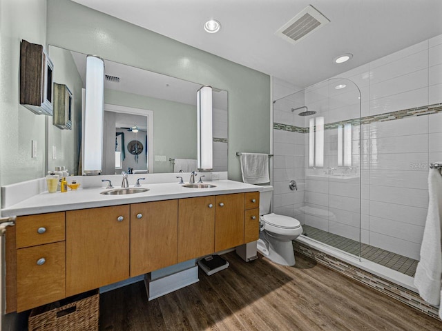 bathroom with wood finished floors, a stall shower, double vanity, and toilet