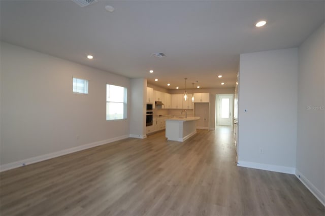 unfurnished living room featuring visible vents, baseboards, recessed lighting, light wood-type flooring, and a sink