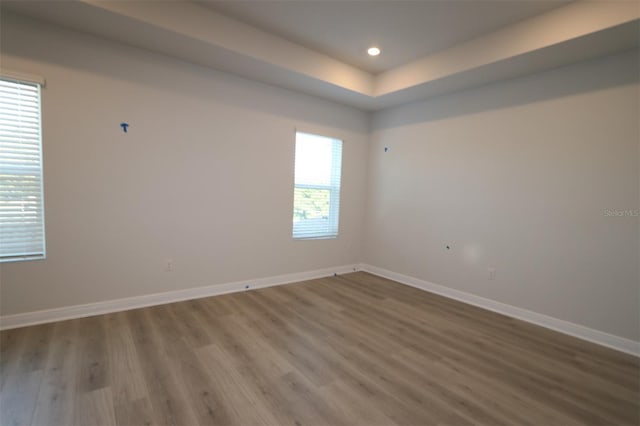 unfurnished room featuring baseboards, a tray ceiling, recessed lighting, and wood finished floors