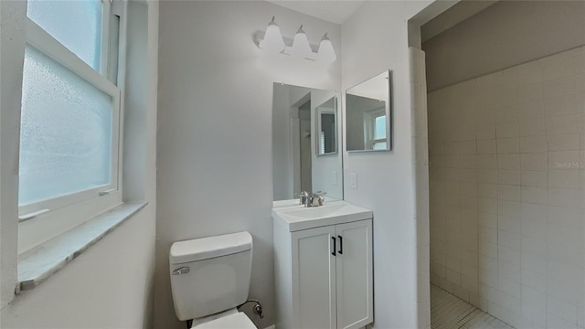 full bathroom with vanity, toilet, tiled shower, and a healthy amount of sunlight