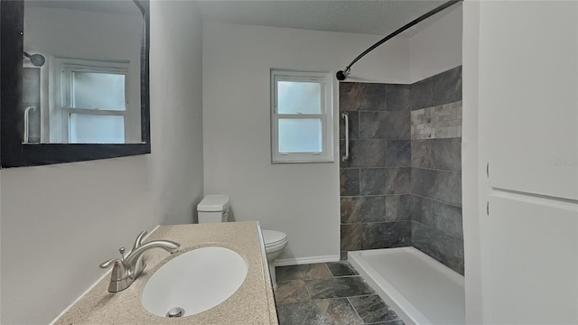 full bath with stone tile flooring, toilet, baseboards, tiled shower, and vanity