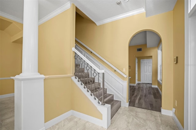 stairway with crown molding, arched walkways, baseboards, and decorative columns
