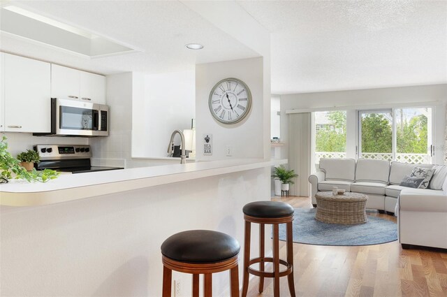 623 Garland Cir, Indian Rocks Beach, FL 33785 - kitchen featuring stainless steel appliances, light wood-style flooring, a breakfast bar, white cabinetry, and open floor plan