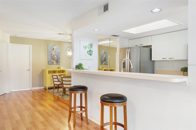 623 Garland Cir, Indian Rocks Beach, FL 33785 - kitchen featuring freestanding refrigerator, a breakfast bar, white cabinets, light wood-style flooring, and a peninsula