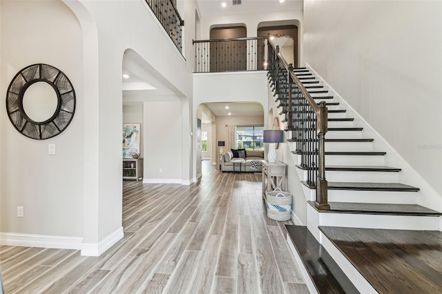 foyer with arched walkways, wood finished floors, stairs, a towering ceiling, and recessed lighting