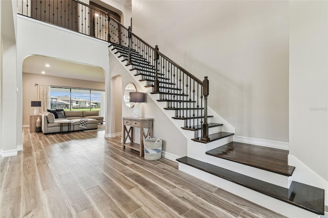 stairs featuring arched walkways, wood finished floors, baseboards, and a high ceiling