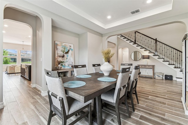 dining room with arched walkways, light wood-style flooring, recessed lighting, baseboards, and stairway