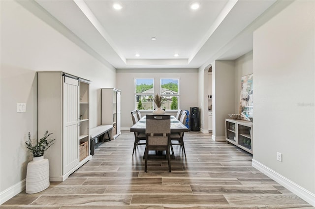 dining space featuring arched walkways, light wood finished floors, recessed lighting, a raised ceiling, and baseboards
