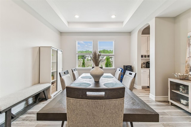dining area with light wood-type flooring, arched walkways, a tray ceiling, baseboards, and recessed lighting