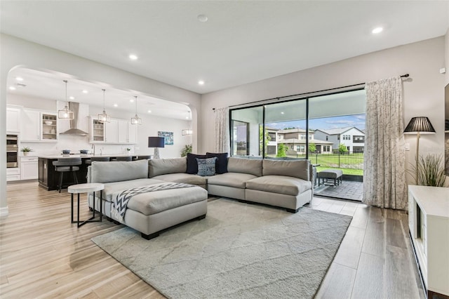 living room with arched walkways, light wood-style flooring, and recessed lighting