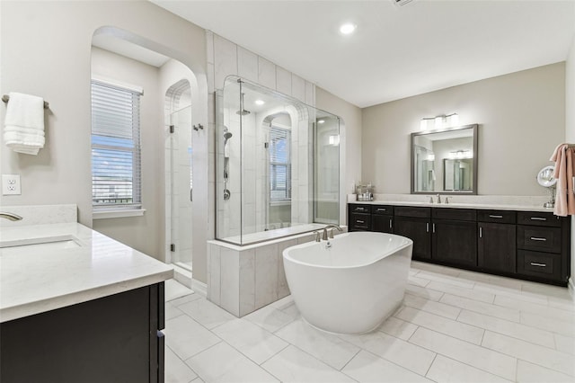 bathroom with a stall shower, two vanities, a soaking tub, and recessed lighting