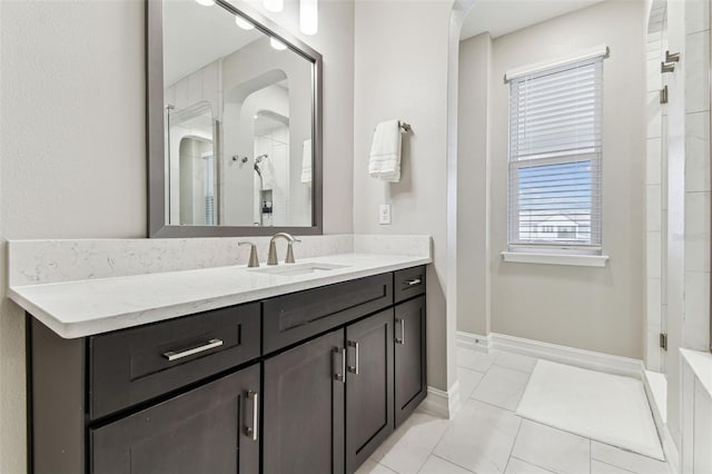 full bathroom with a tile shower, vanity, and baseboards