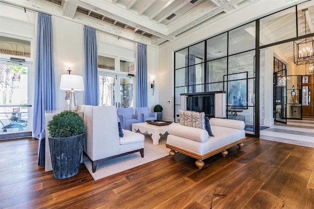 living room with hardwood / wood-style flooring, a towering ceiling, a chandelier, and beam ceiling