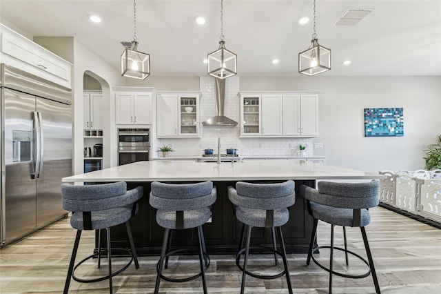 kitchen with stainless steel appliances, wall chimney exhaust hood, light countertops, tasteful backsplash, and light wood-style floors