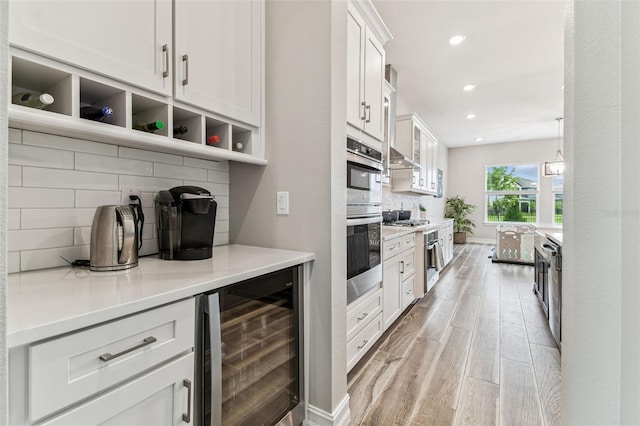 kitchen featuring beverage cooler, light wood-style flooring, decorative backsplash, white cabinetry, and recessed lighting