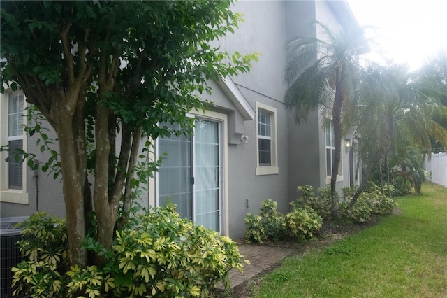 view of home's exterior featuring a lawn, fence, central air condition unit, and stucco siding