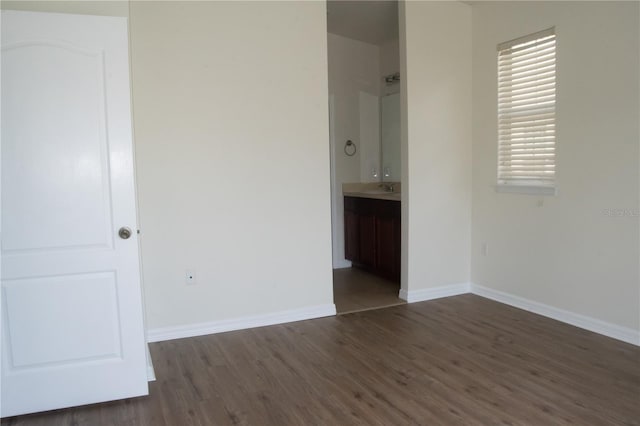 unfurnished bedroom with a sink, baseboards, ensuite bathroom, and wood finished floors
