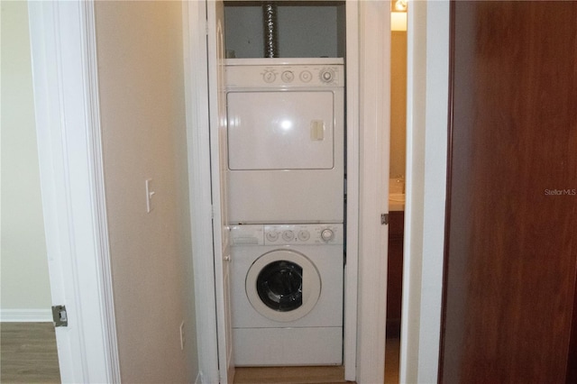 clothes washing area with stacked washer and clothes dryer, wood finished floors, and laundry area