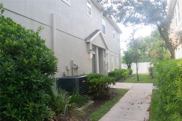 view of side of home with central AC, fence, and stucco siding