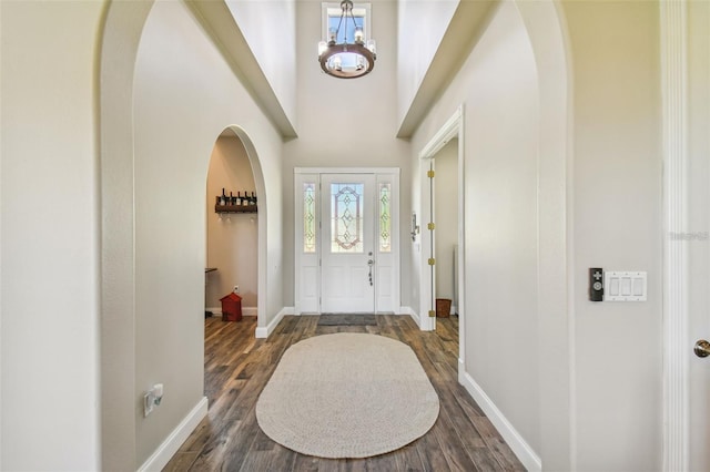 entrance foyer featuring arched walkways, baseboards, a chandelier, and dark wood-style floors