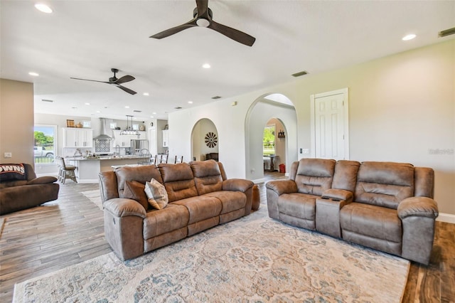 living area with arched walkways, ceiling fan, recessed lighting, and light wood-type flooring
