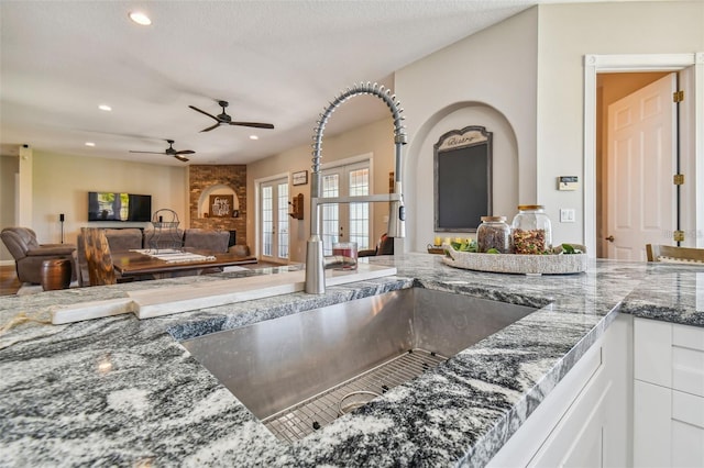 kitchen featuring open floor plan, recessed lighting, dark stone counters, white cabinetry, and a sink