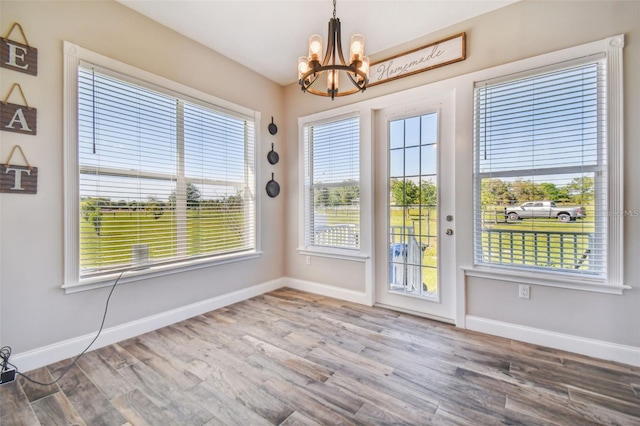 unfurnished dining area featuring an inviting chandelier, baseboards, and wood finished floors