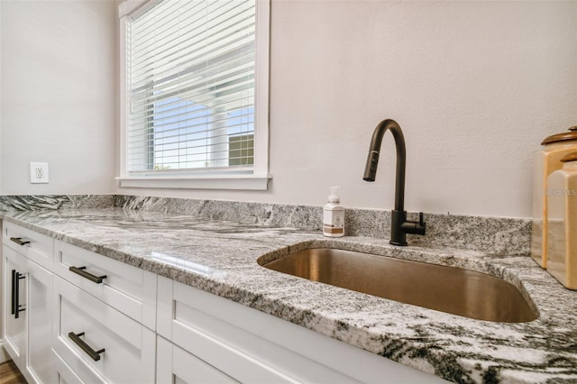 room details with white cabinets, light stone countertops, and a sink