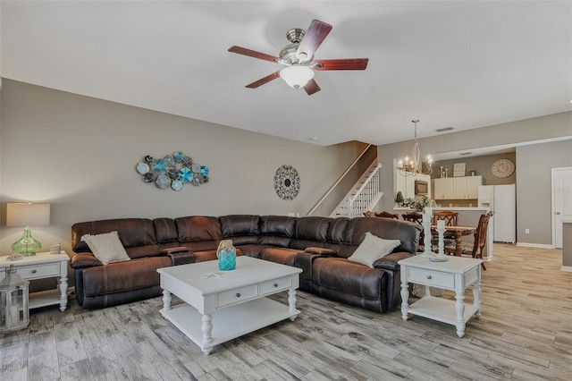 living room with ceiling fan with notable chandelier, stairs, baseboards, light wood-type flooring, and visible vents