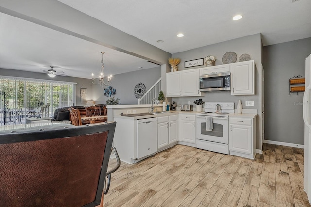 kitchen featuring a peninsula, white appliances, light wood-type flooring, white cabinetry, and a sink