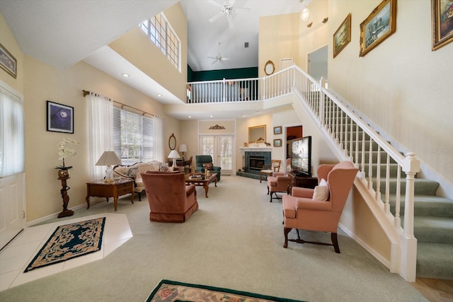 living area with a high ceiling, a fireplace with raised hearth, stairs, and ceiling fan