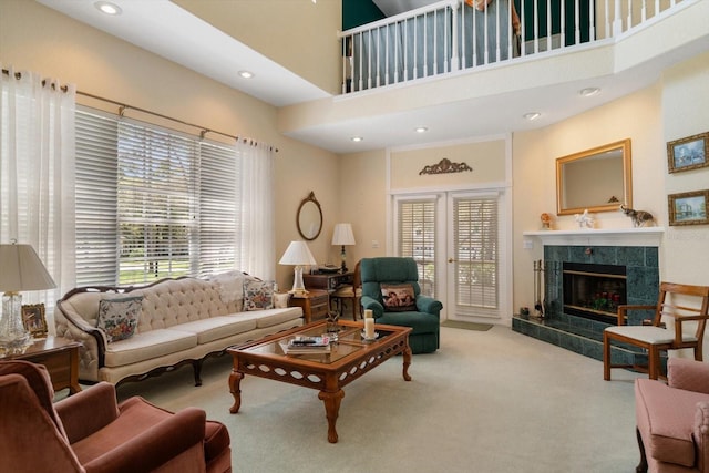carpeted living area with a tiled fireplace, recessed lighting, and a high ceiling