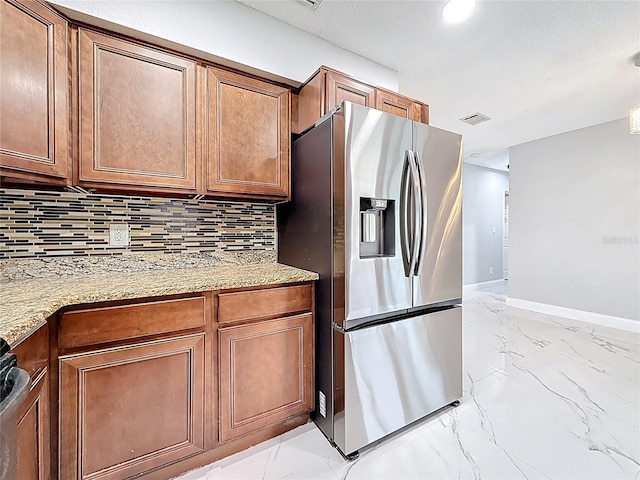 kitchen featuring marble finish floor, visible vents, stainless steel fridge, brown cabinets, and tasteful backsplash