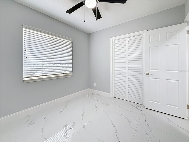 unfurnished bedroom with a ceiling fan, a closet, baseboards, and marble finish floor