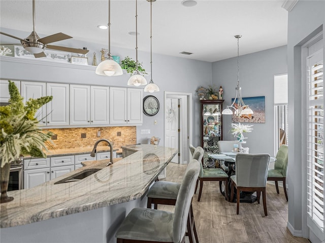 2908 89th Ave E, Parrish, FL 34219 - kitchen with a sink, decorative backsplash, light stone countertops, white cabinets, and a ceiling fan