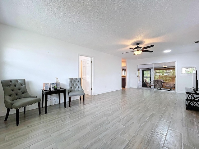 living area with baseboards, ceiling fan, wood finish floors, and a textured ceiling