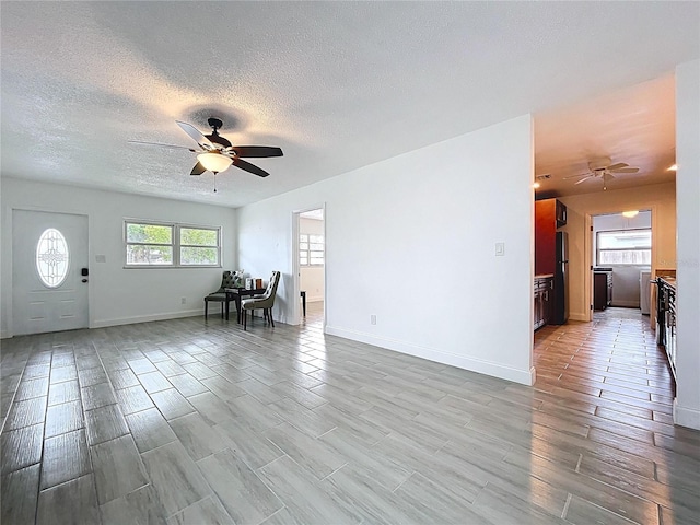 unfurnished living room with baseboards, a ceiling fan, and a textured ceiling