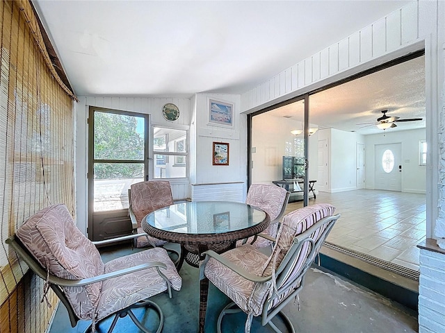 dining space with wooden walls, concrete flooring, ceiling fan, and vaulted ceiling