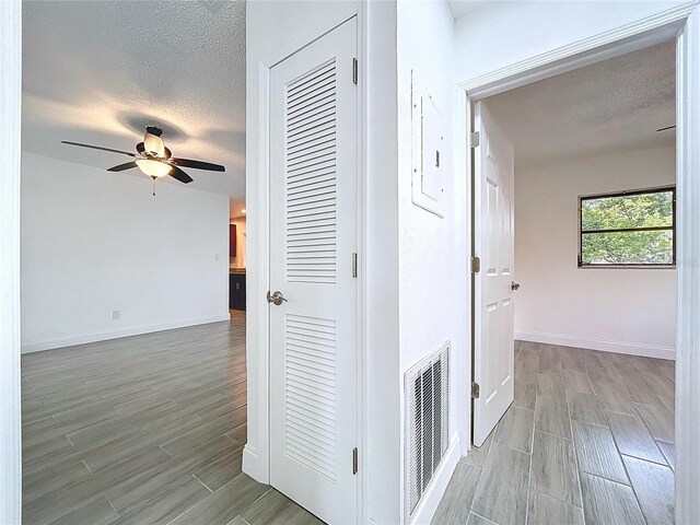 hallway with visible vents, a textured ceiling, and wood finish floors