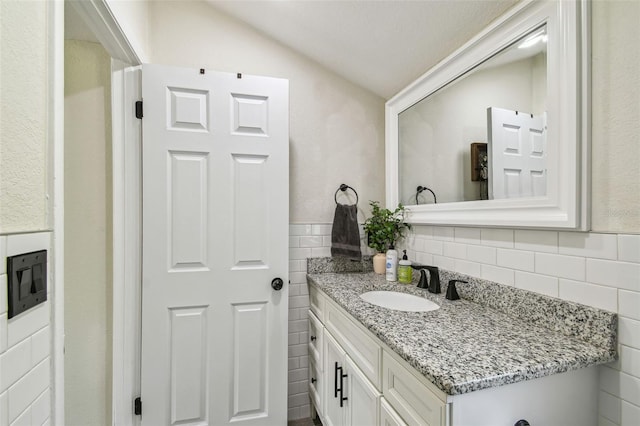 bathroom featuring vanity, lofted ceiling, and tile walls