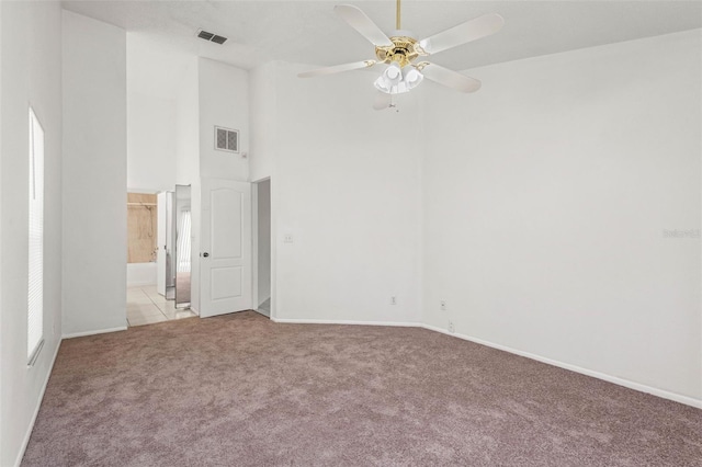 spare room with visible vents, a towering ceiling, light carpet, baseboards, and ceiling fan