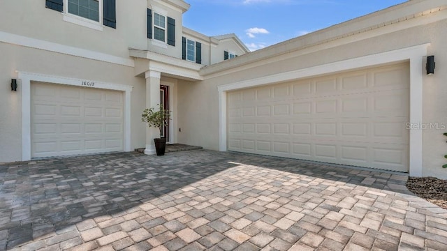view of front of house featuring decorative driveway, an attached garage, and stucco siding